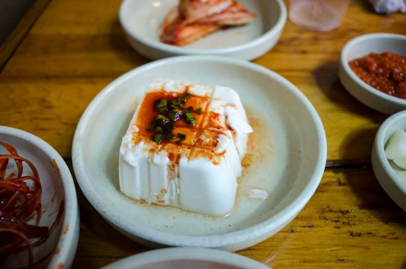 Silken tofu topped with chili oil, next to small side dishes
